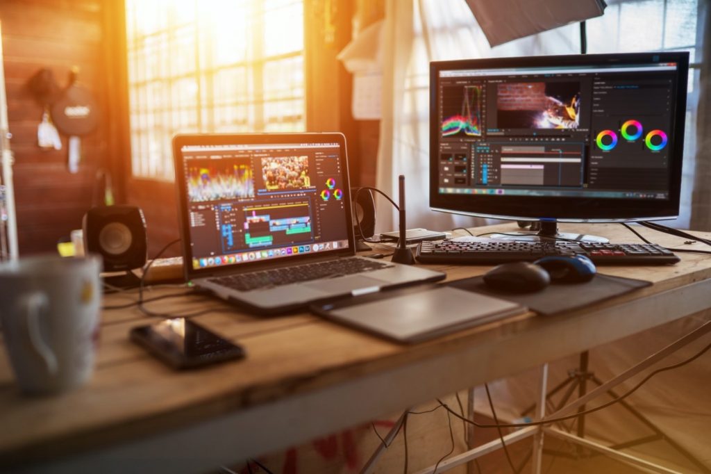 A computer sitting on top of a table connected to a monitor with video editing software.